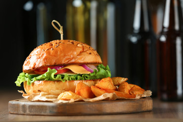 Wooden board with tasty burger and fried potatoes on table