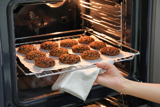 Woman taking baking tray with delicious oatmeal cookies out of oven