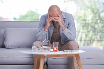 Drunk depressed man sitting on sofa at home. Alcoholism concept