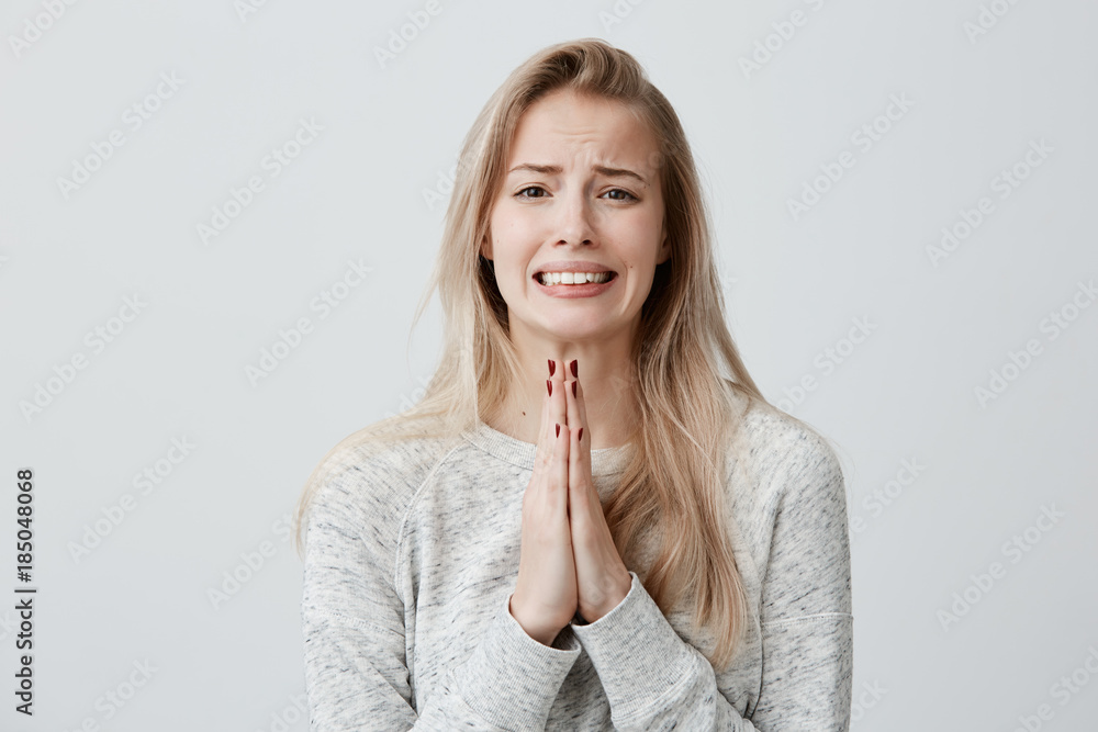 Wall mural beautiful blonde female clenching teeth with begging look holding palms pressed together in front of - Wall murals