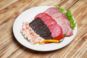 Plate with different cut sausages and lard on wooden table