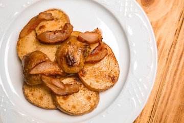 Obraz na płótnie Canvas Plate with tasty fried potato and bacon crisps on wooden table, closeup