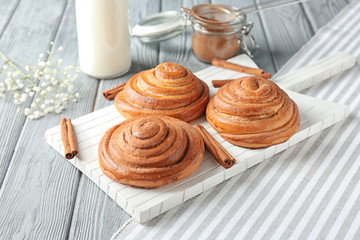Wooden board with sweet cinnamon rolls on table