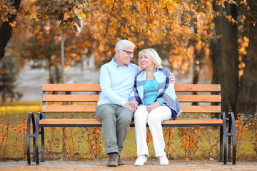 Cute elderly couple sitting on bench in autumn park