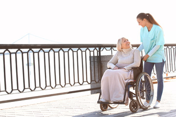 Disabled senior woman and young caregiver outdoors