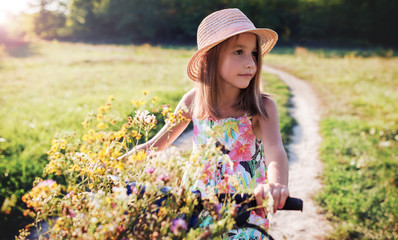 Obraz premium Cute little girl riding a bike with flowers in the basket. Nature, lifestyle