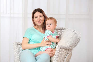 Young mother with baby sitting in armchair indoors