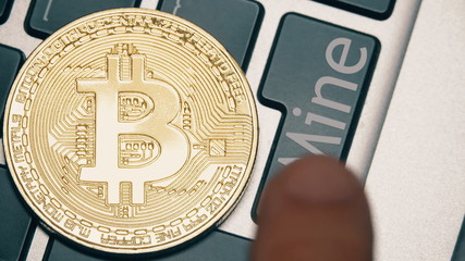 Shiny bitcoin on the computer keyboard and the Mine button being pressed