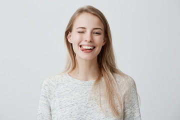 Gloomy young blonde woman with dyed hair dressed casually making faces at camera, blinking,...