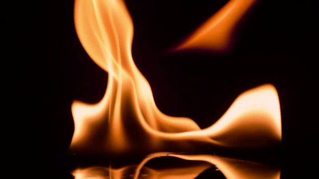 Fire and flames burning on a reflective glass surface, in slow motion with a black background, with the flames moving slowly and extinguishing at the end