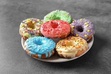 Plate with yummy colorful donuts on grey background