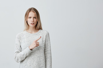 Beautiful woman with blonde dyed hair looking at something with disgust and dissatisfaction...