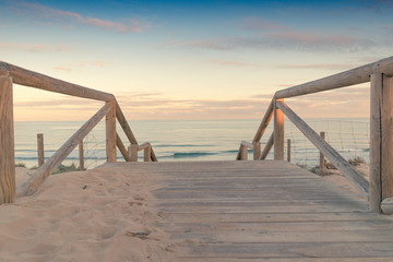 Wooden staircase and railing access to the beach sand at sunset with somewhat cloudy sky an sea with waves in Guardamar, Spain