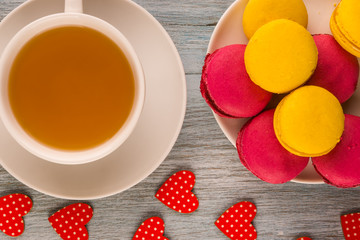 A cup of tea and cakes Macaron close-up on a rustic wooden background with hearts