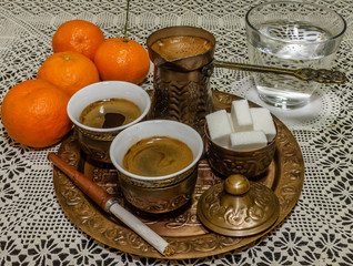 Turkish coffee served with a coffee pot,sugar cubes,glass of water with tangerines and cigarette holder on white doily