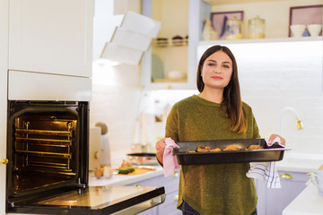 Portrait of the young cheerful woman who standing in the kitchen and holding baked dish in hands