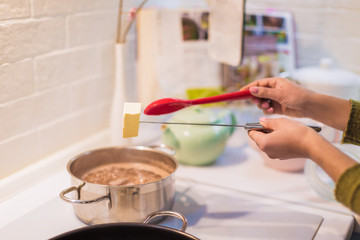 Close-up the young woman throw butter in saucepan in the kitchen