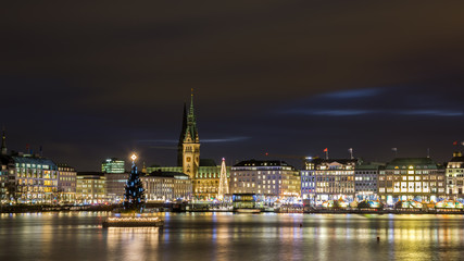 Fototapeta na wymiar Christmas in Hamburg. Panoramic view of the decorated city center from Alster Lake, view to Hamburg Rathaus and a christmas tree installed in the center of the lake. Atmosphere before the New Year. 