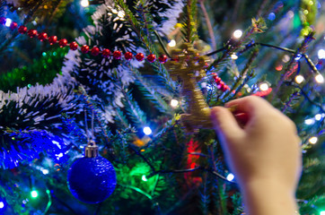 Dziecko wiesza ozdoby na choince bożonarodzeniowej. Widać dłoń dziecka i kolorowe lampki i...