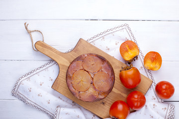pie with persimmon on a brown wooden board on a white background and a white tablecloth