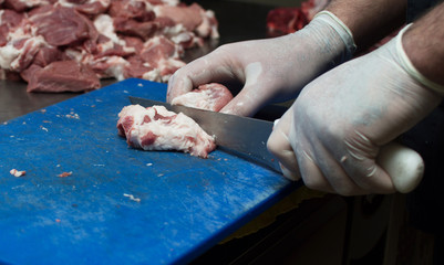 The butcher cuts a piece of pork in the kitchen with a sharp knife. A cook in white gloves is cutting meat.
