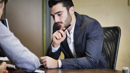 Handsome businessman sitting in his office, talking to client and showing him options on tablet PC screen.