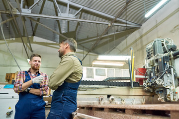 Obraz na płótnie Canvas Portrait of two workmen chatting while operating machines in modern industrial shop standing by cutting unit, copy space