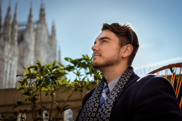 Young elegant man sitting on the chair in cafe-terrace in beautiful winter day in Milan. One Person