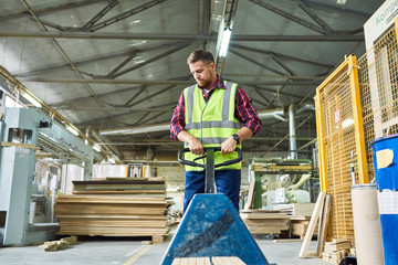 Portrait of young man wearing reflective jacket pulling cart in factory warehouse, copy space