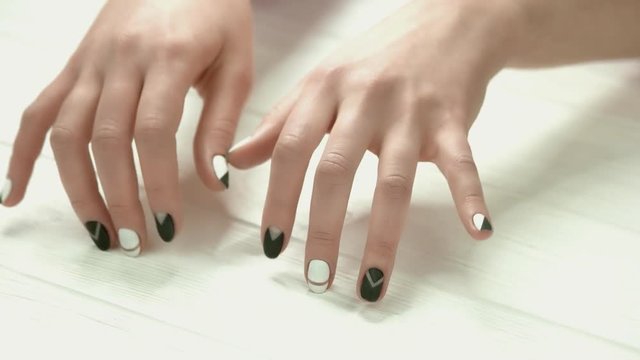 Manicured hands knocking on table. Young woman hands with black and white matte manicure close up.
