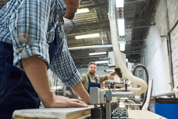 Side view  of two workmen wearing in overalls working in factory shop operating modern machines, copy space