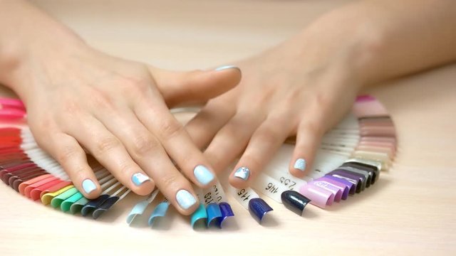 Woman hands and nail samples collection. Well-groomed female hands covered with gentle blue polish and nail color palette. Beautiful winter manicure.