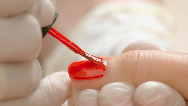 Manicurist accurately applying varnish on nail. Cosmetician in rubber gloves covering female finger nails with red color polish. Women beauty and care.