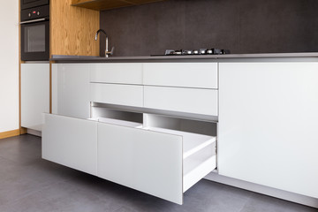 Opened kitchen drawer, kitchen in a modern loft style with wooden elements, grey ceramic countertop and tile backsplash.