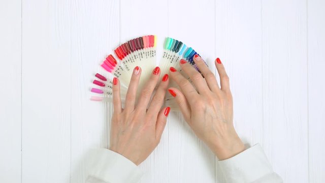 Hands and nail color samples, top view. Red manicure with romantic design and nail colors palette on table in beauty salon.