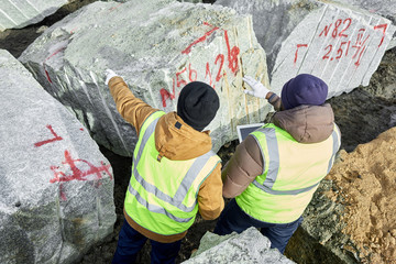 Obraz na płótnie Canvas High angle of two industrial workers wearing reflective jacket marking piece of granite on mining worksite outdoors