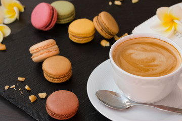 Colorful macaroons on black stone background with a cup of aromatic coffee.