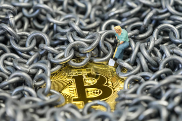 Bitcoin mining by miniature figure holding shovel digging on shiny golden physical Bitcoin Crpto currency coin surround by metal chains or blockchain concept