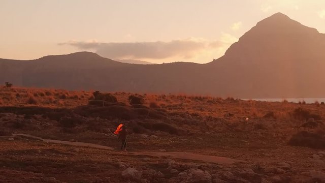 Magestic mountain pic at the sunset. The little girl figure is walking near it. She is holding a red kite. 