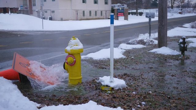 Yellow Fire hydrant spraying water out onto road in winter