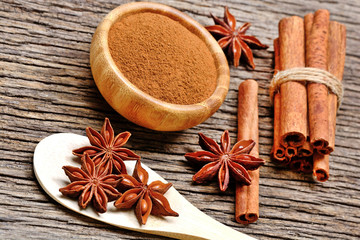 Wooden spoon with anise star and cinnamon powder with sticks on table