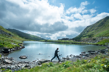 Traveler with trekking poles walks on the shore of a mountain lake