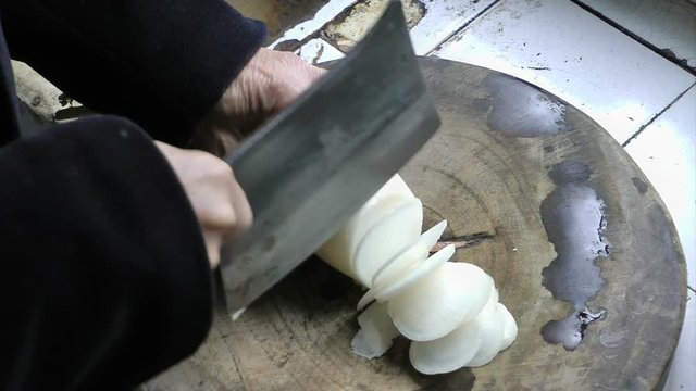 An old man cuts the radish with a Chinese kitchen knife