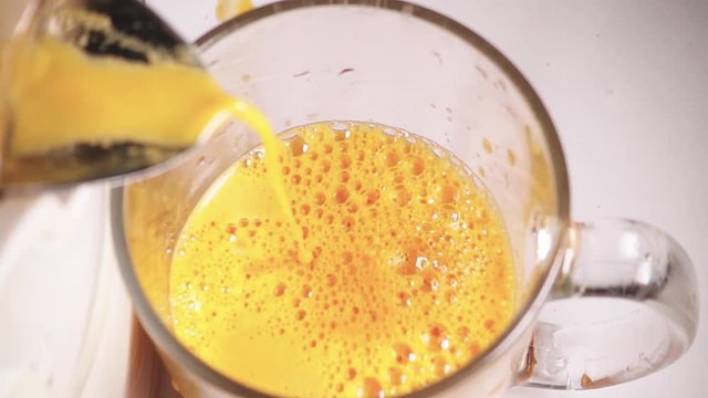 Fresh squeezed carrot juice is poured into the cup, slow motion
