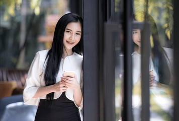 Smiling attractive caucasian businesswoman using smartphone near glass wall with reflection