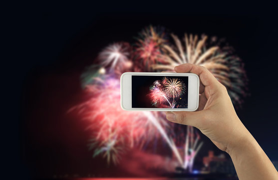 hand of a businessman holding a smartphone to take a pictures at night and fireworks on dark sky.