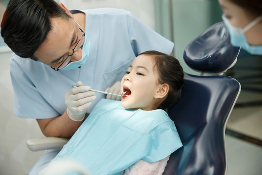 The dentist and the dentist's assistant are examining the tooth for the little girl