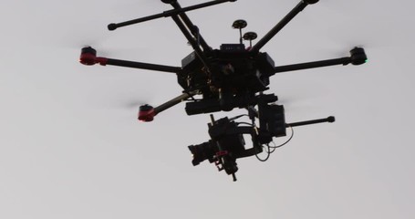 Large drone with camera flying towards sunny sky