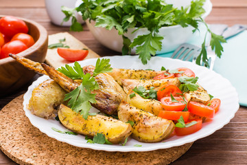 Baked chicken wings and potatoes, fresh tomatoes and greens on a plate