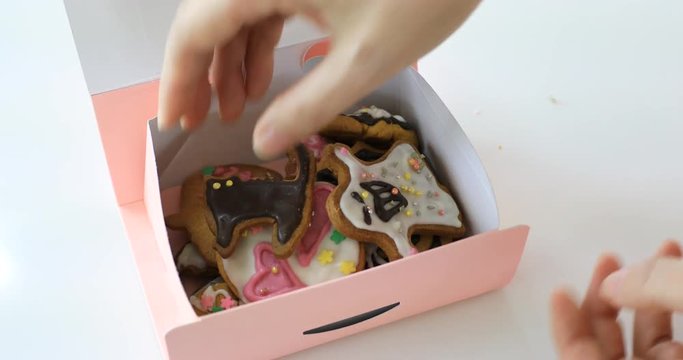 Hand putting ghost halloween cookies into pink gift box and closing a lid 